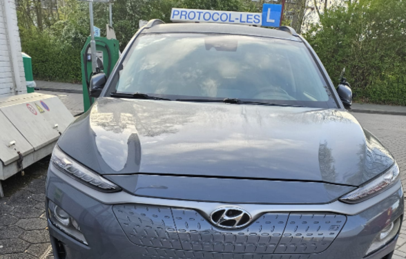Grijze Hyundai Kona Electric lesauto met dakbord Protocol-Les en L-bord